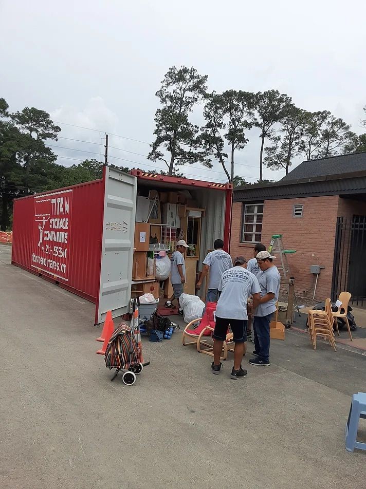 Group of people organizing and moving items from an open red shipping container next to a brick building.